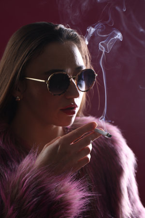 Woman in fur coat smoking cigarette on pink background, closeupの写真素材