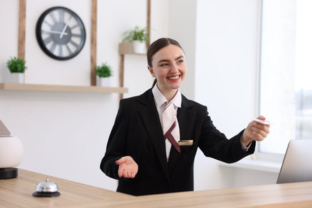 Smiling receptionist in uniform giving card key at reception desk in hotelの写真素材