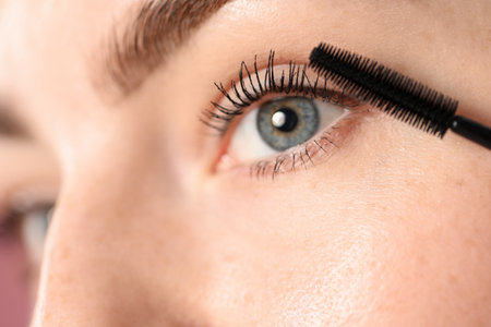 Young woman applying mascara onto her eyelashes, closeupの写真素材