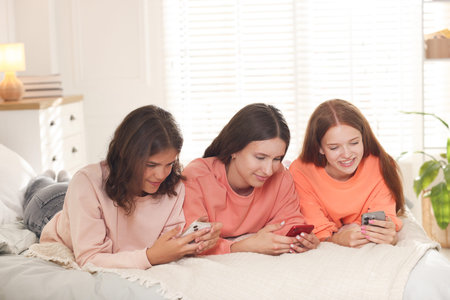 Friends with smartphones on bed at home