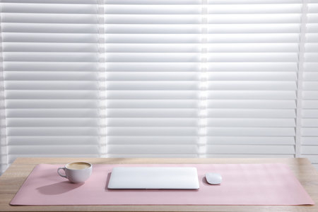 Stylish workplace with laptop and pink mousepad on wooden table indoors. Space for text