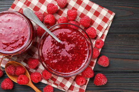 Sweet raspberry jam in glassware and berries on wooden table, flat lay