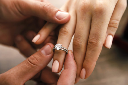 Making proposal. Man putting engagement ring on his girlfriend's finger indoors, closeup