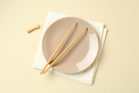 Stylish plate, chopsticks and napkin on beige background, flat lay