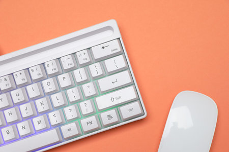 Modern white keyboard with RGB lighting and mouse on orange background, top view