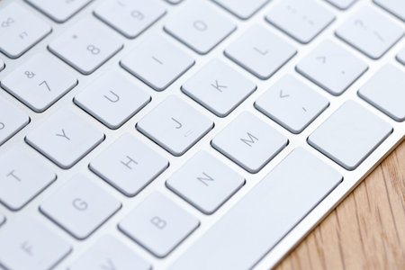 Modern white wireless keyboard on wooden table, closeup