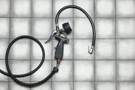 One tire inflation gun with gauge on light tiled background, top view