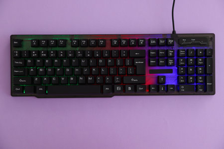 Modern computer keyboard with RGB lighting on violet background, top view