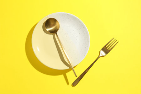 Stylish plate and cutlery on yellow background, flat lay