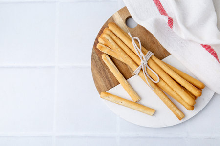 Delicious grissini sticks on white tiled table, top view. Space for text
