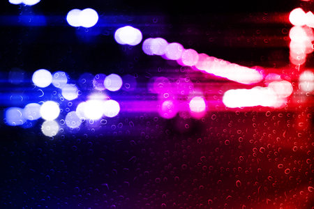 Red and blue lights in city at night, blurred view through wet glass