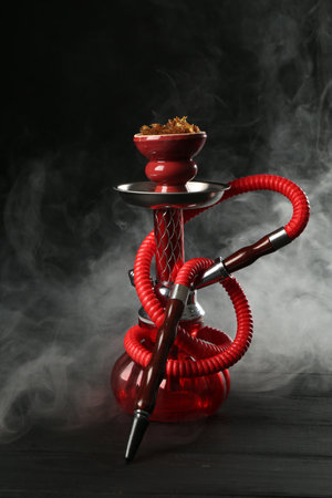 Hookah on wooden table with smoke against black backgroundの写真素材