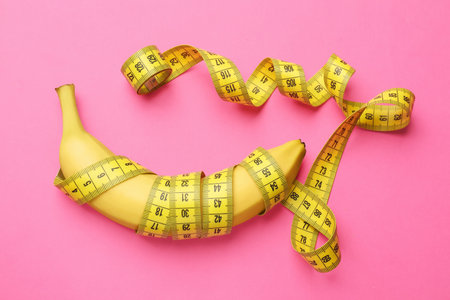 Banana with measuring tape on pink background, top view