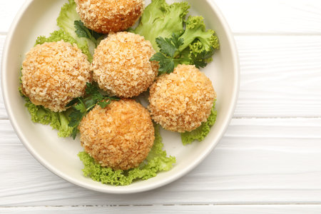 Delicious fried croquette balls with parsley and lettuce on white wooden table, top view