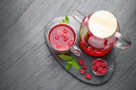Aromatic raspberry tea in glass cup, teapot, berries and mint on black table, top view. Space for textの写真素材