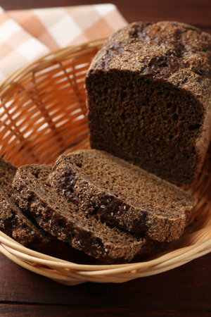 Pieces of fresh rye bread in wicker basket on wooden table, closeup