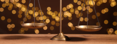 Golden scales of justice on wooden table against blurred lights, closeupの写真素材