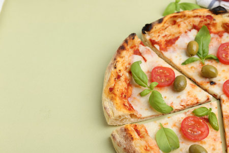 Delicious cut pizza with tomatoes, basil and olives on light green background, closeup. Space for...