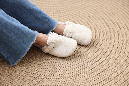 Woman in soft white slippers on wicker mat, closeup