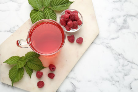 Aromatic raspberry tea in glass cup, berries and green leaves on white marble table, top view. Space...
