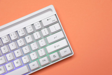 Modern white keyboard with RGB lighting on orange background, top view. Space for text