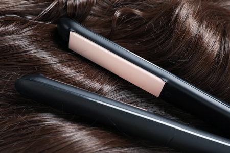 Modern flat iron on shiny brown hair, closeup