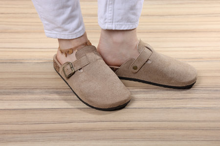 Woman in stylish beige slippers on wooden floor, closeup