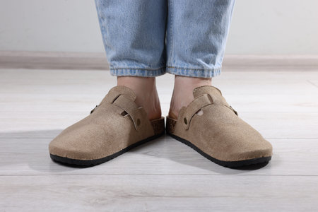 Woman in stylish beige slippers on light wooden floor, closeup