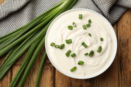 Tasty sour cream in bowl and green onions on wooden table, flat layの写真素材