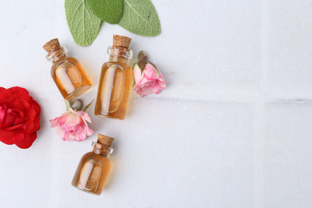 Bottles of cosmetic products, roses and sage on white table, flat lay. Space for textの写真素材