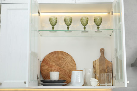 Clean dishware and glasses on shelves in cabinet indoors