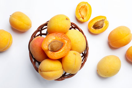 Fresh apricots and wicker basket on white background, flat lay