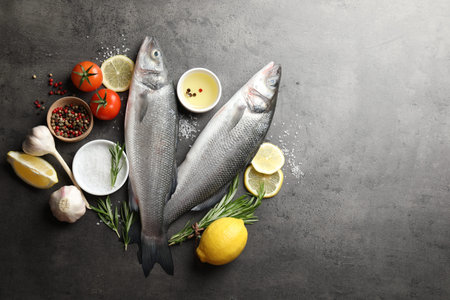 Fresh raw seabass fish with spices on grey table, flat lay and space for text. Seafood delicacies