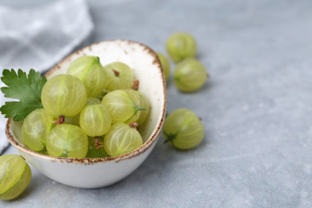 Fresh green gooseberries in bowl on grey table, closeup. Space for textの写真素材