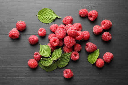 Tasty fresh ripe raspberries and leaves on black table, flat lay