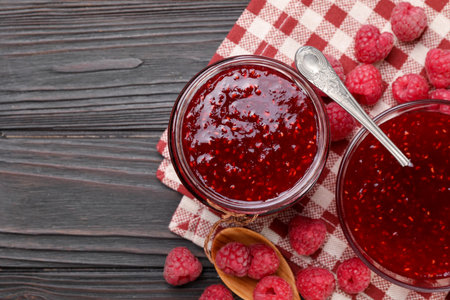 Sweet raspberry jam in glassware and berries on wooden table, flat lay. Space for text