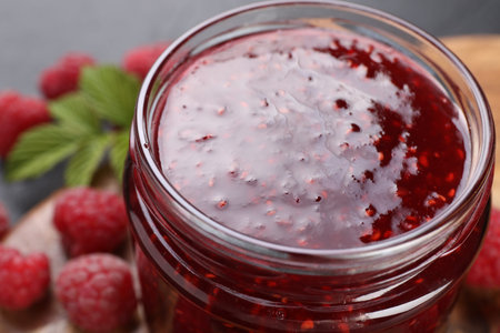Sweet raspberry jam in glass jar and berries on table, closeup