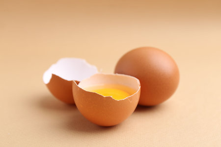 Whole and broken chicken eggs on beige background, closeup