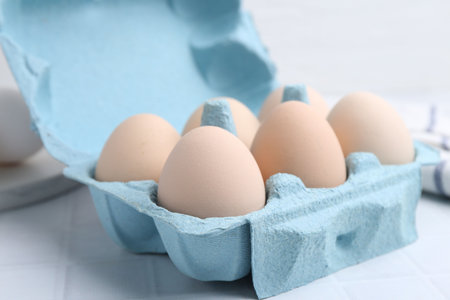 Raw chicken eggs in egg carton on white tiled table, closeup