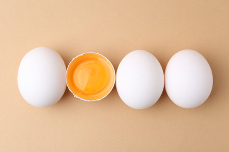 Whole and broken chicken eggs on beige background, top view