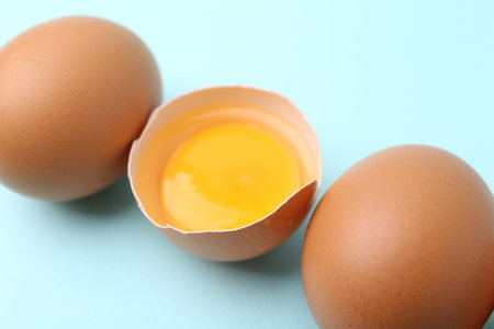 Whole and broken chicken eggs on light blue background, closeup