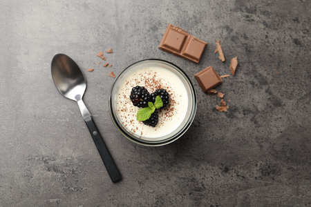 Tasty panna cotta with blackberries, mint and chocolate pieces on grey table, flat lay