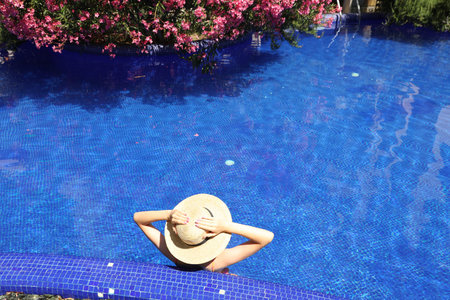 Girl with straw hat in swimming pool outdoors on sunny day, above view