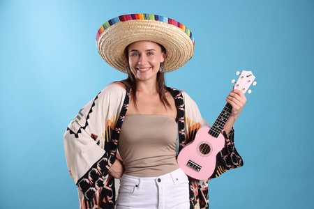 Happy woman in sombrero hat with ukulele on light blue backgroundの写真素材