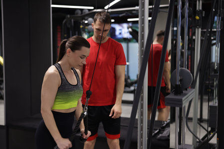 Young woman exercising with lat pulldown machine with professional personal trainer in gym