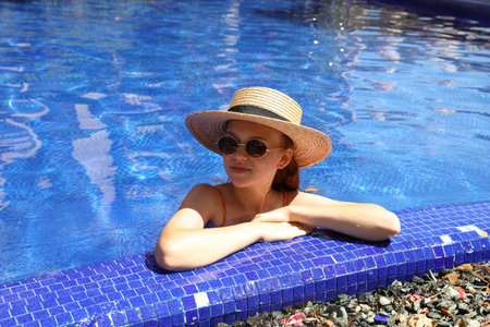 Girl with straw hat in swimming pool outdoors on sunny day