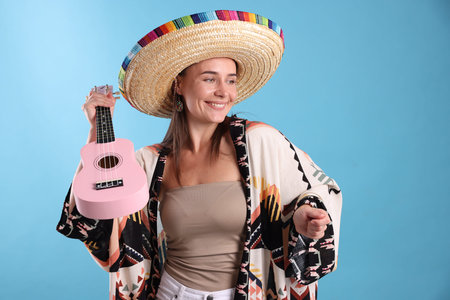 Happy woman in sombrero hat with ukulele on light blue backgroundの写真素材