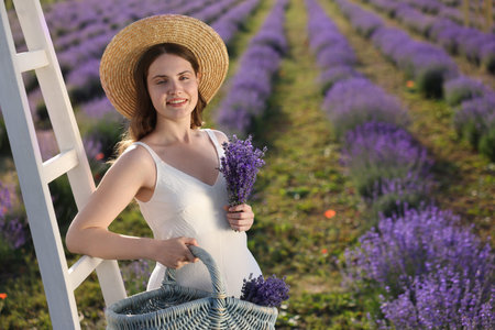 Beautiful young woman with lavender flowers and wicker basket in field