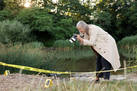 Forensic expertise. Detective with camera working at crime scene near lake outdoors, space for text