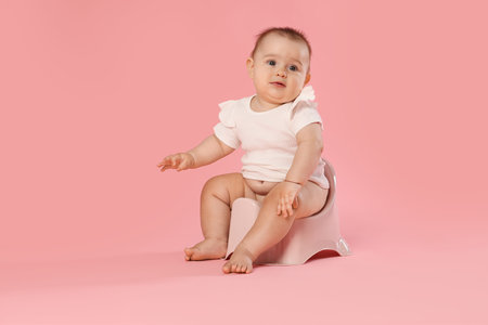 Cute little baby sitting on potty against pink background